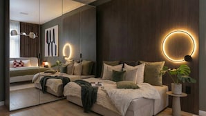A modern bedroom with a large mirror, a bed with multiple pillows, a bedside table with a lamp, and a round wall light. - TurnKey | Top-Floor 3BR for 12 in central Prague (Praha 2)