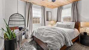 Ein Schlafzimmer mit Holzboden, einem Bett mit grauer Decke, einem Hängestuhl und einem Blumentopf.