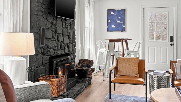 Ein gemütliches Wohnzimmer mit Kamin aus Stein, einem an der Wand befestigten Flachbildfernseher und einem Essbereich mit weißen Stühlen und einem Tisch.