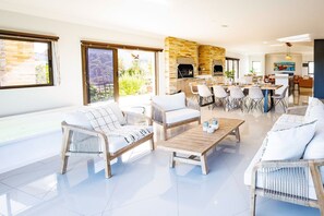 A spacious living area with a dining table, multiple sofas, and a kitchen area with a stone wall and grill. - Langebaan Country Estate (Langebaan)