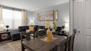 A modern living room with a dark grey sofa, a wooden dining table, and a vase of flowers. - Newly Renovated 3BR in Kingston’s Desirable West End | The Yellow Door Retreat (Kingston)