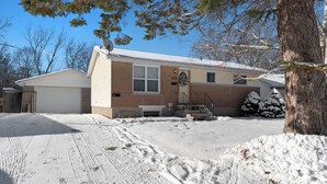A two-story house with a garage, a front porch, and a snow-covered driveway. - Newly Renovated 3BR in Kingston’s Desirable West End | The Yellow Door Retreat (Kingston)
