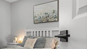 A bedroom with a bed, a nightstand, a wall-mounted painting, and a door. - Newly Renovated 3BR in Kingston’s Desirable West End | The Yellow Door Retreat (Kingston)