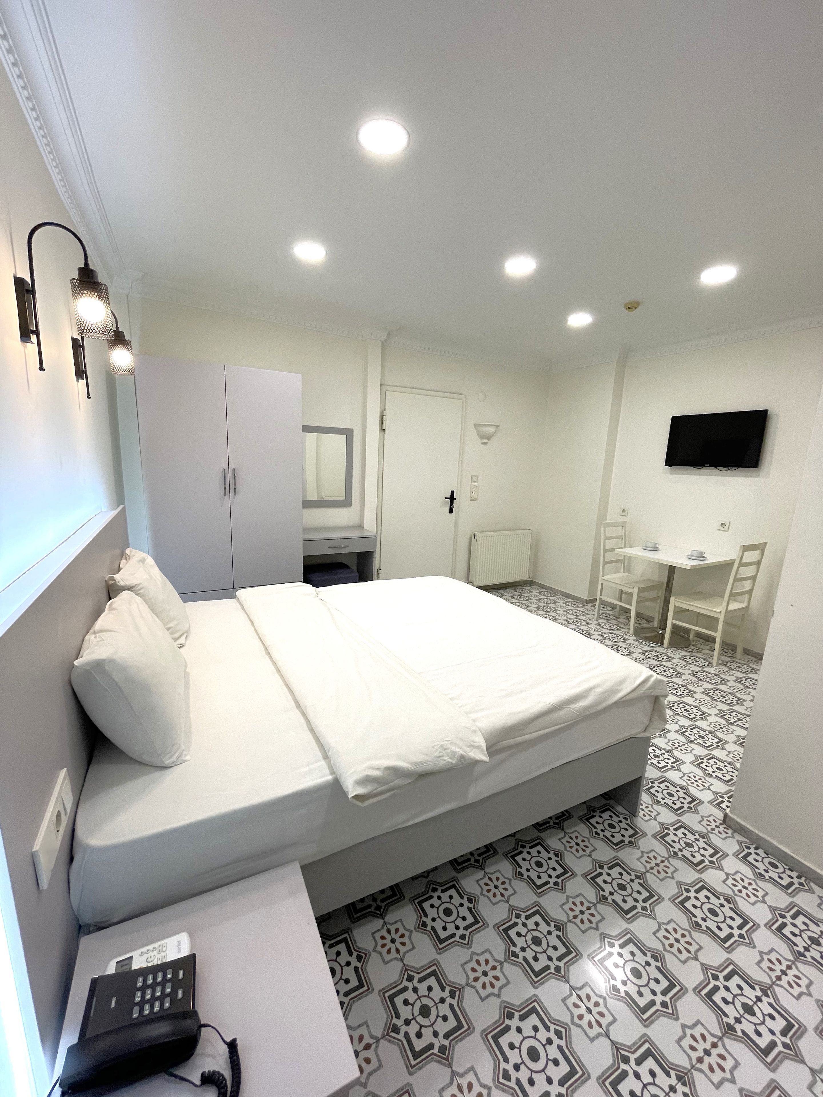A hotel room with a bed, a desk, a chair, a wardrobe, a mirror, a television, and a telephone.