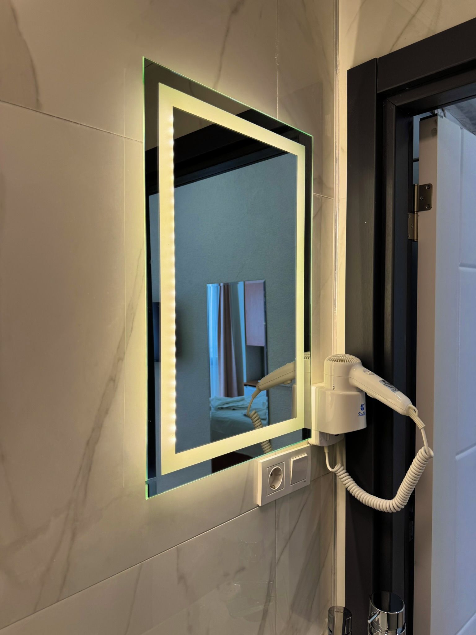 Ein Badezimmer mit Schminkspiegel, Fön und Handtuchhalter.