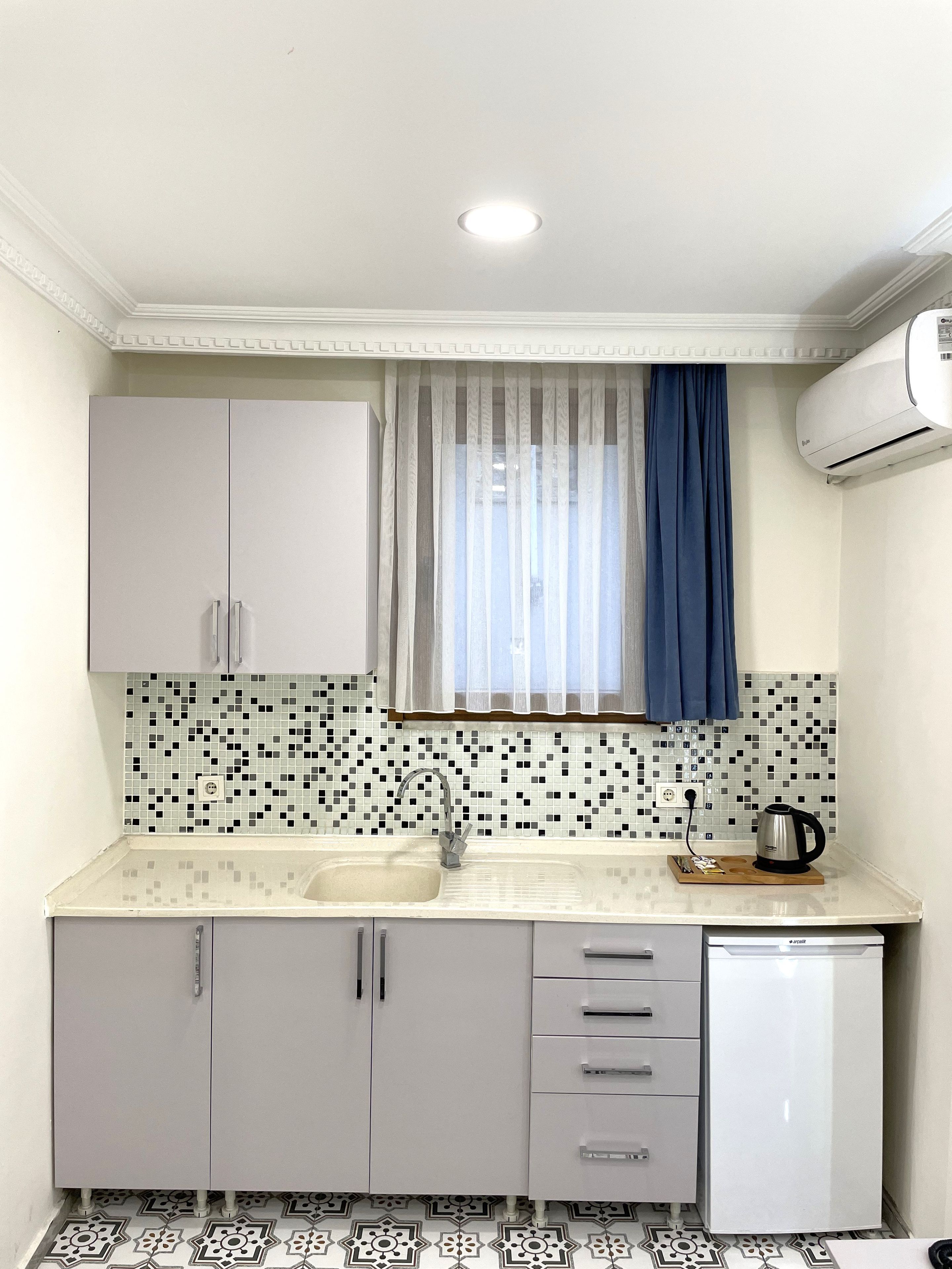 A compact kitchen with a sink, a small refrigerator, and a window with curtains.