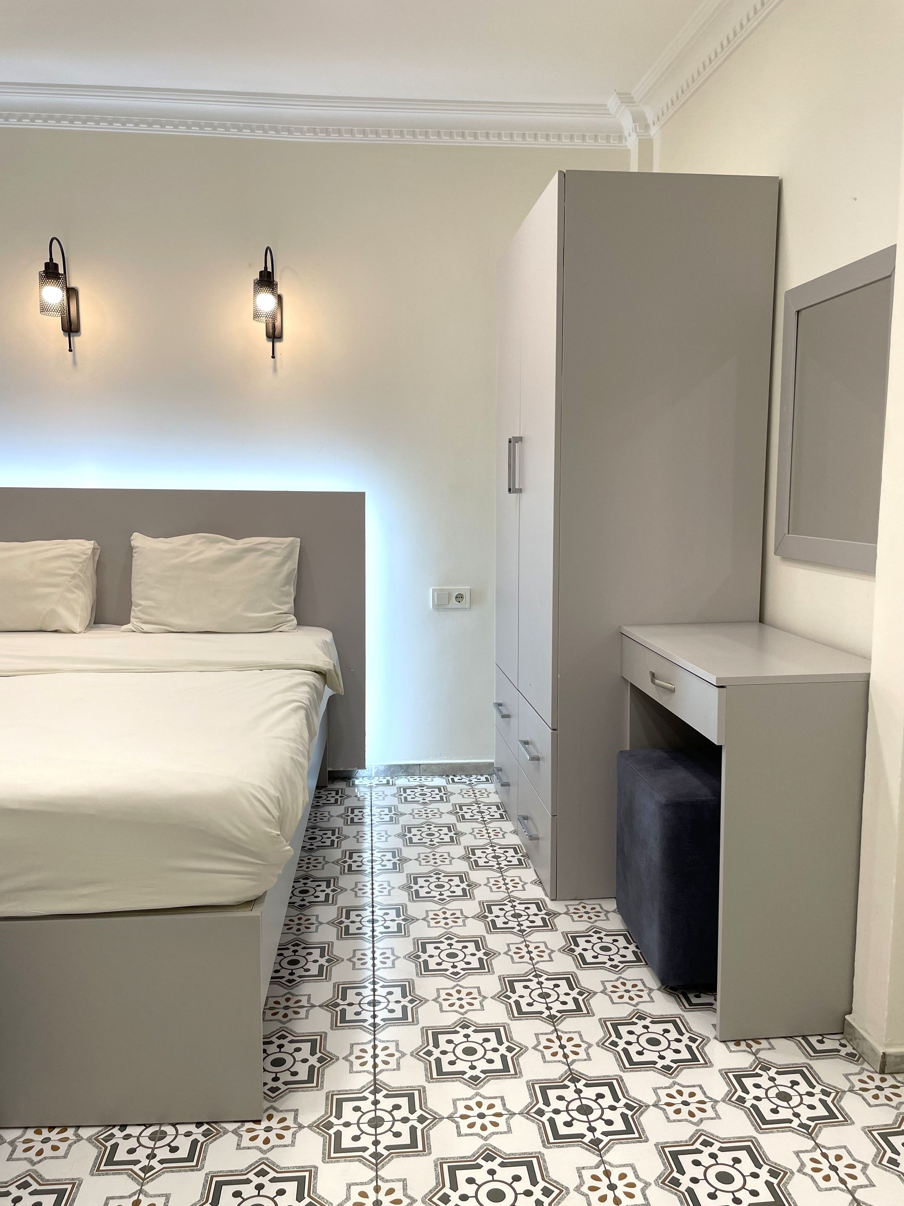 Un dormitorio con cama, lámparas de noche, cómoda y baldosas de suelo estampadas.