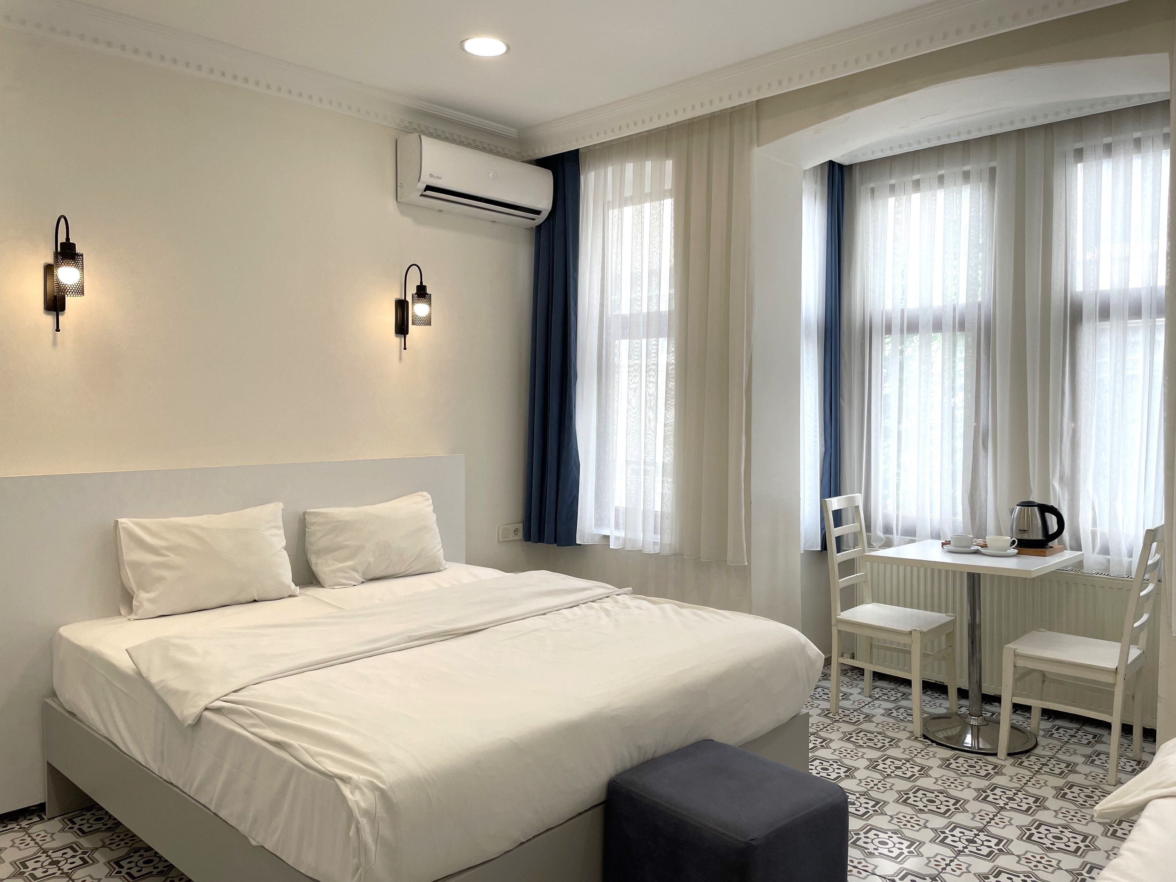 Ein Hotelzimmer mit einem großen Bett, zwei Wandleuchten, einer Klimaanlage, einem kleinen Tisch mit einem Stuhl und einem Heizkörper.