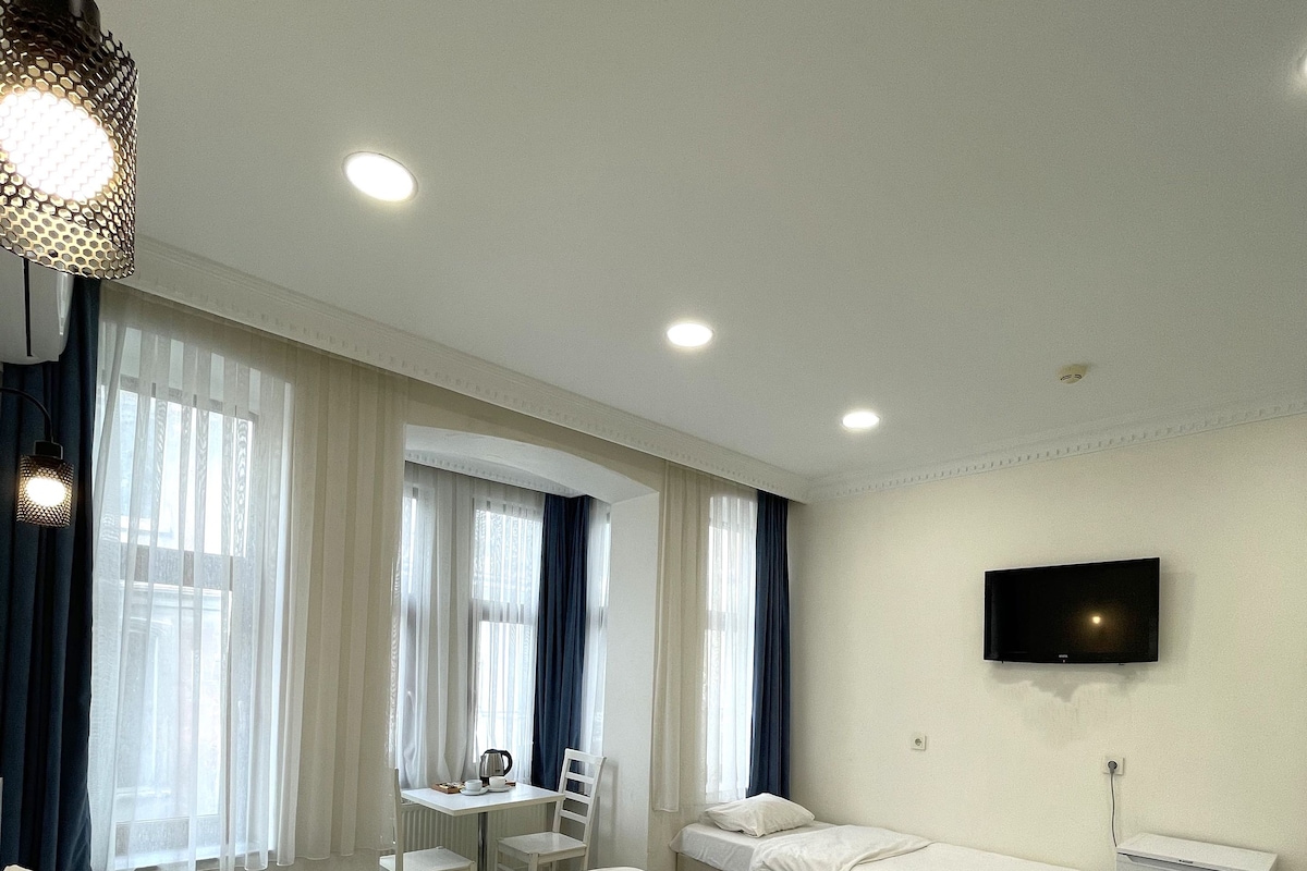 Quarto de hotel com duas camas, uma escrivaninha, uma cadeira, televisão e um pequeno frigorífico.