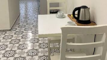 Ein schmaler Flur mit fugenreichen Bodenfliesen, einem weißen Tisch mit Kaffeemaschine und einem Stuhl.