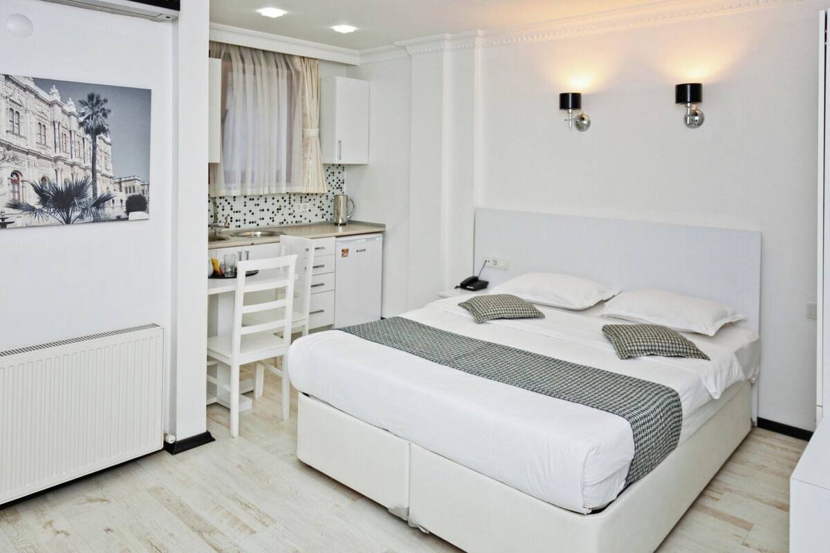A bedroom with a bed, bedside table, and a view of the kitchen.