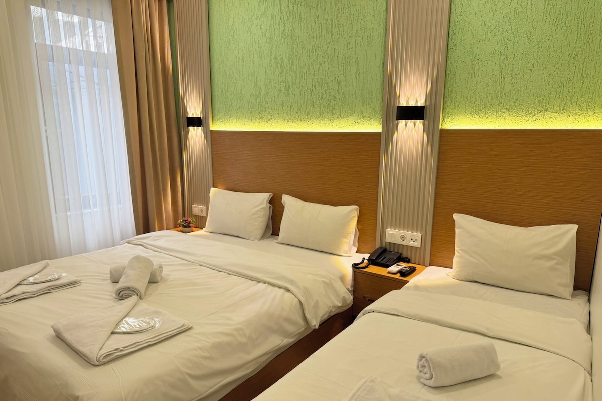 Quarto de hotel com duas camas, cada uma com toalhas bem dobradas, um telefone ao lado da cama e uma mesinha de cabeceira.