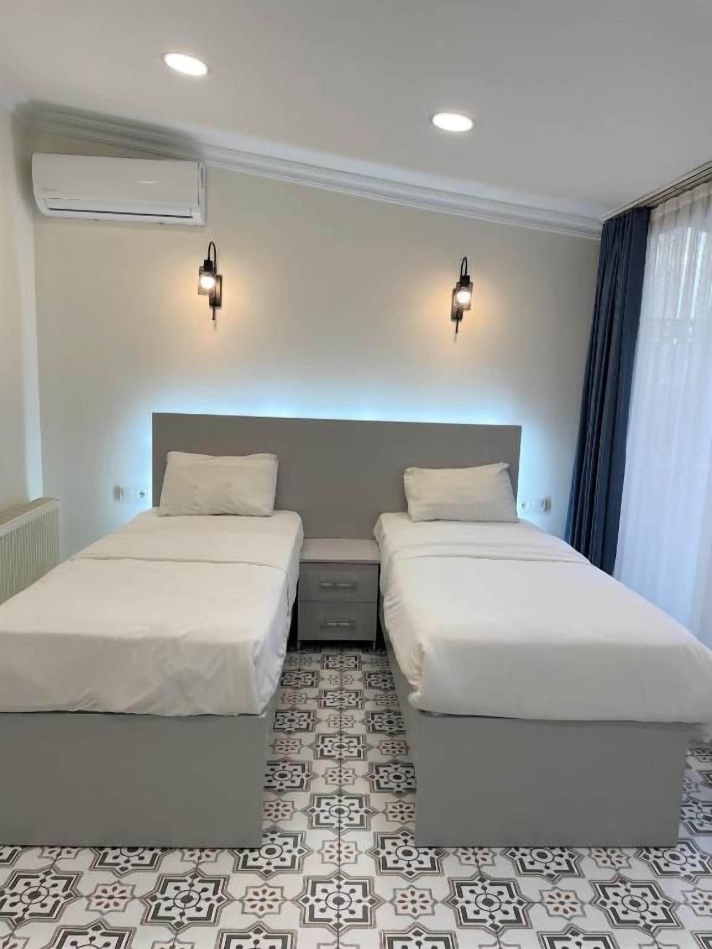 Een hotelkamer met twee enkele bedden, een nachtkastje, een airconditioning en vloertegels met een patroon.