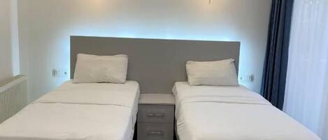 Een hotelkamer met twee enkele bedden, een nachtkastje, een airconditioning en vloertegels met een patroon.