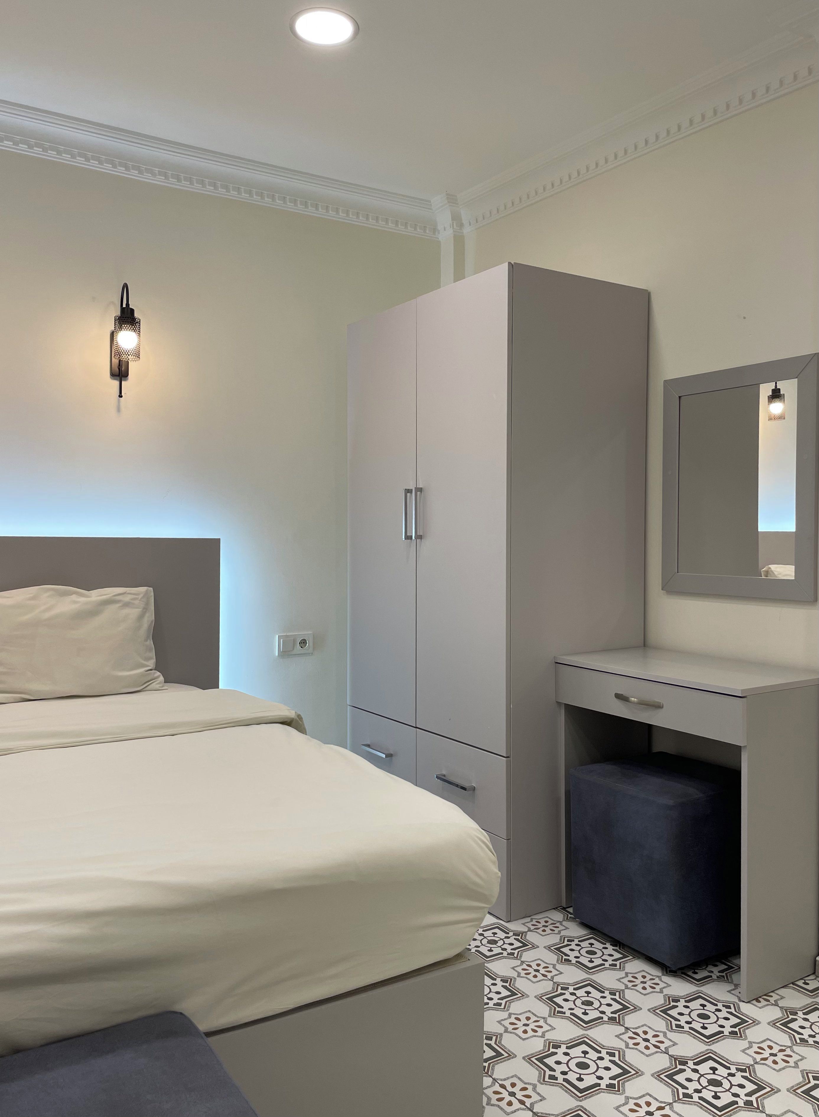 A bedroom with a bed, a wardrobe, a desk, and a mirror.