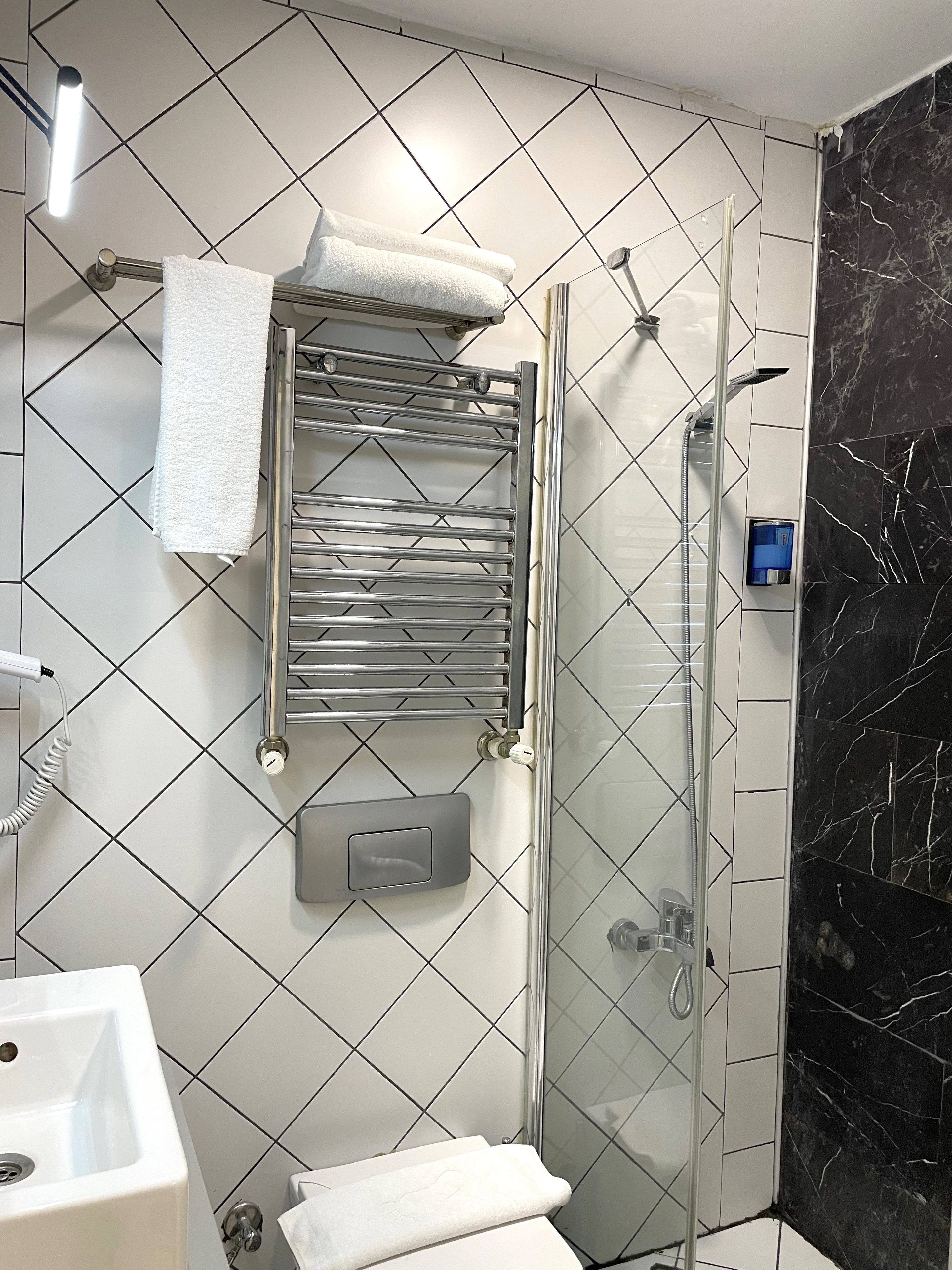 Un baño con ducha, toallero y secamanos.