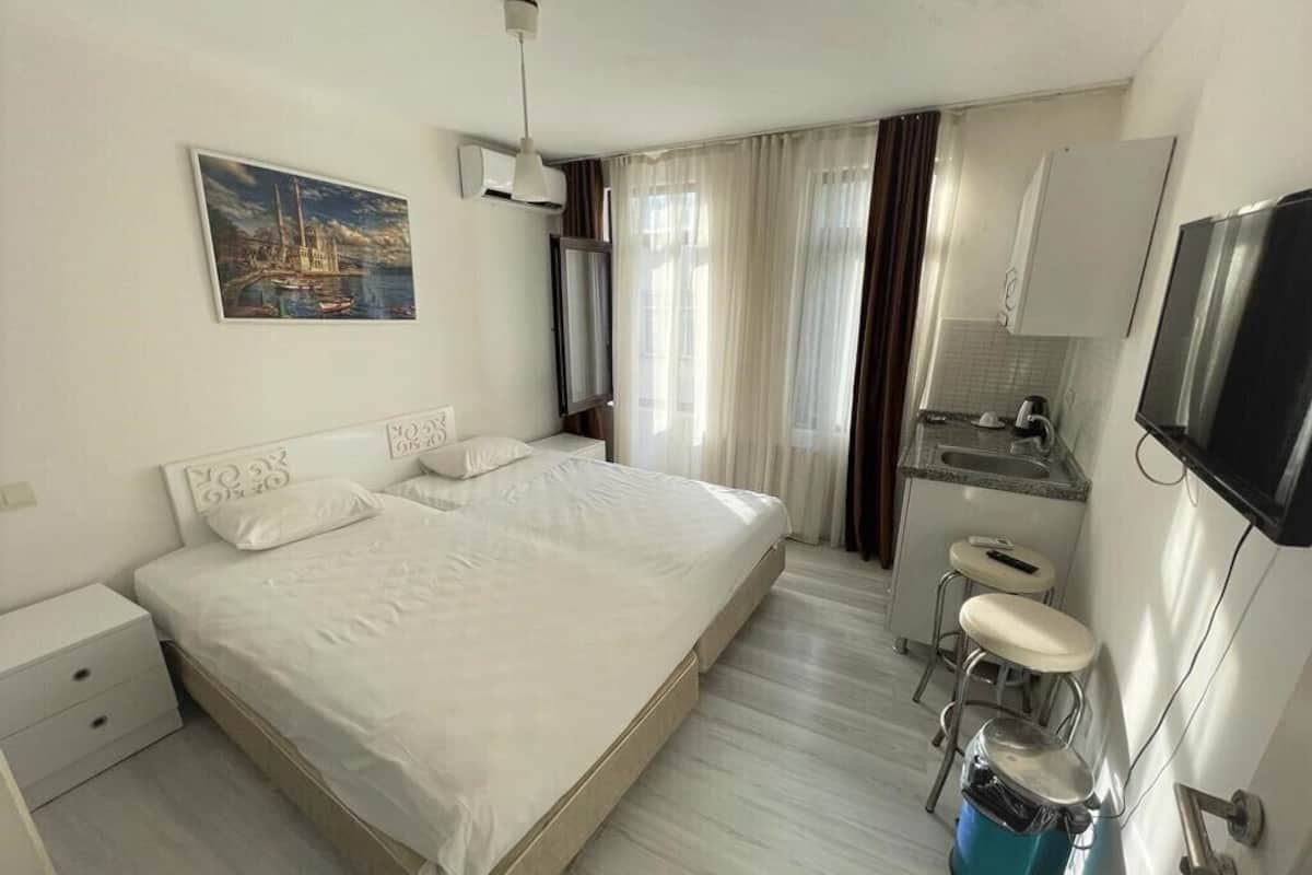 A hotel room with a large bed, a small kitchenette, a TV, and a painting on the wall.