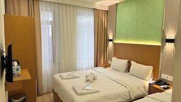 Ein Hotelzimmer mit zwei Betten, einem Holzschrank, einem Schreibtisch mit Telefon und Lampe sowie einer Wand in Grünton.