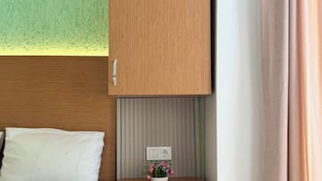 A hotel room with a bed, a small wooden cabinet, a mini fridge, a power outlet, and a potted plant.