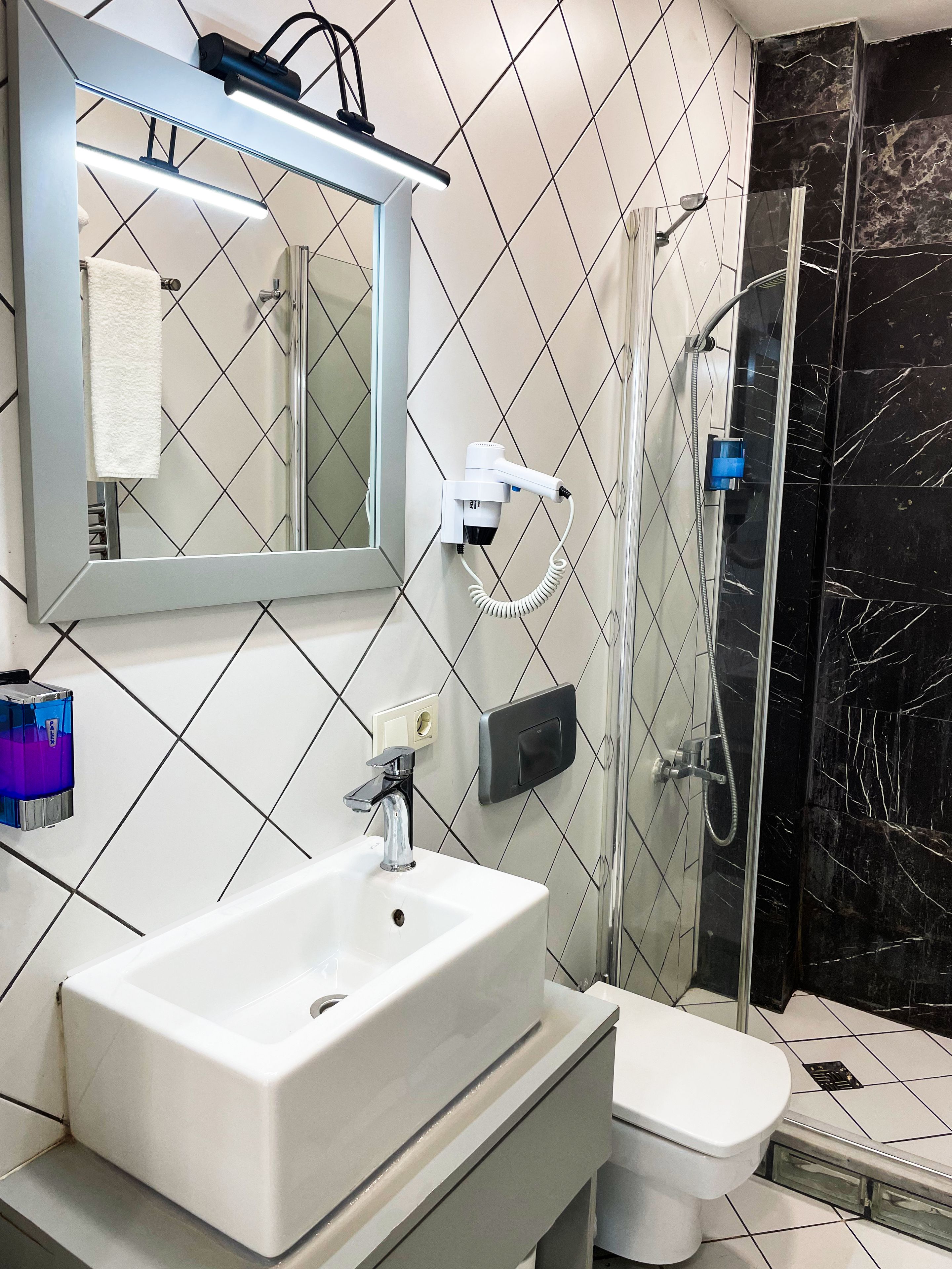 Ein Badezimmer mit einem weißen Waschbecken, einem Spiegel, einem Handhaartrockner und einer Dusche mit Glastür.