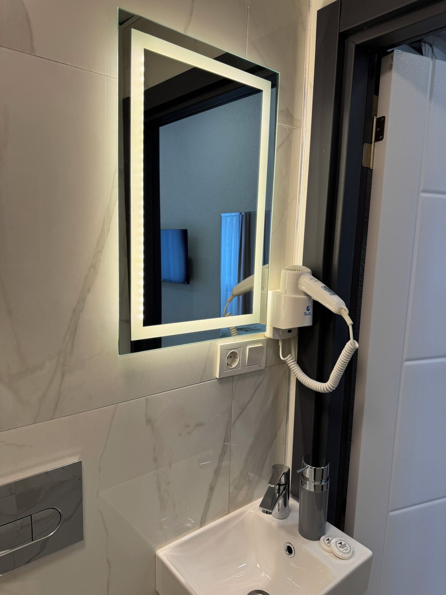 Un bagno con un lavandino bianco, uno specchio con luce integrata e un asciugacapelli.