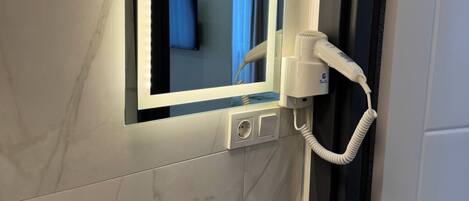 Un bagno con un lavandino bianco, uno specchio con luce integrata e un asciugacapelli.