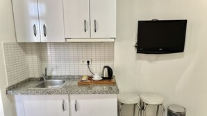 A small kitchenette with white cabinets, a granite countertop, a sink, a kettle, and a black TV mounted on the wall. - Royal Pera Taksim (Istanbul)
