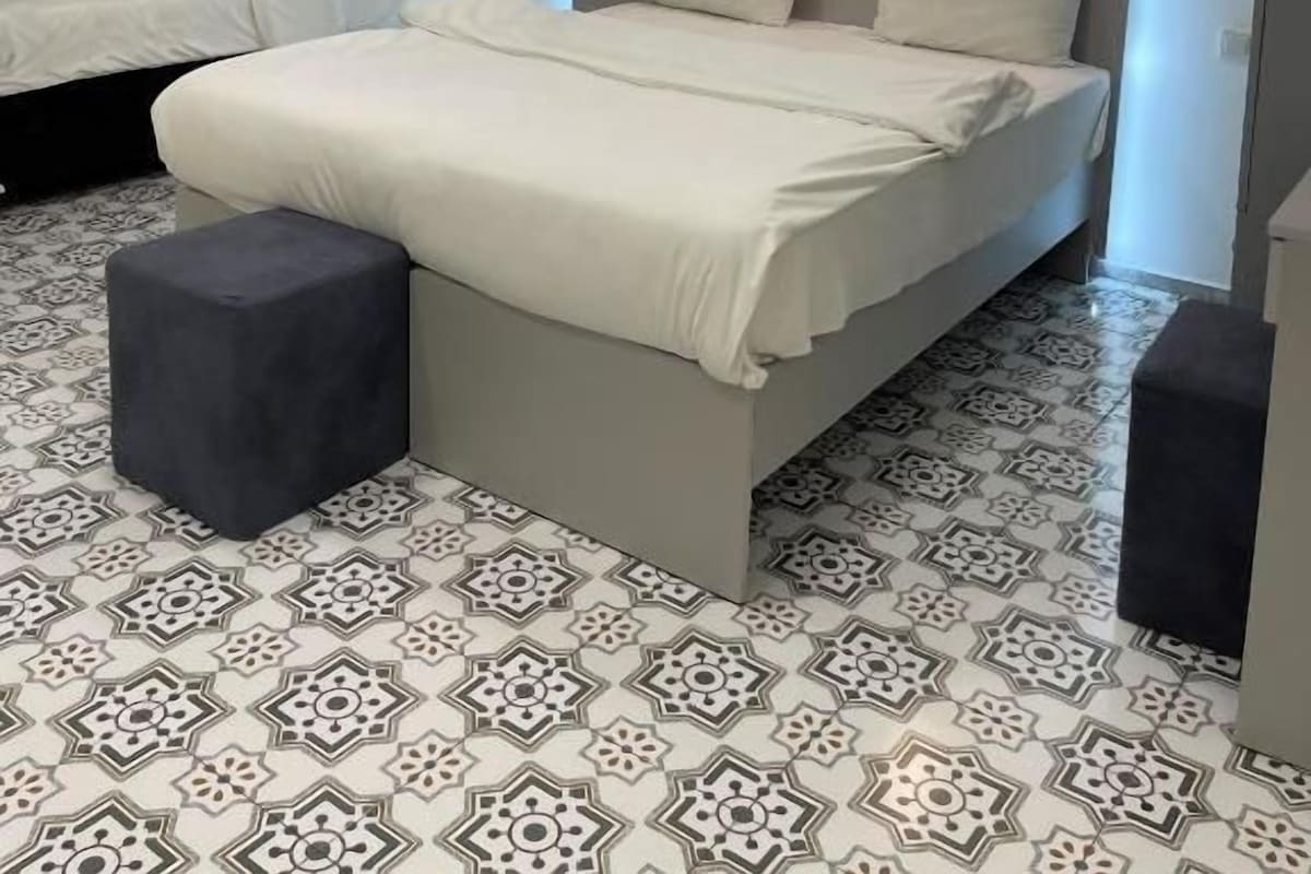 Quarto moderno com uma cama grande, duas mesas de cabeceira e uma cama menor ao fundo.