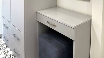A corner bedroom with a grey wardrobe, a bedside table, a mirror, and a patterned floor.