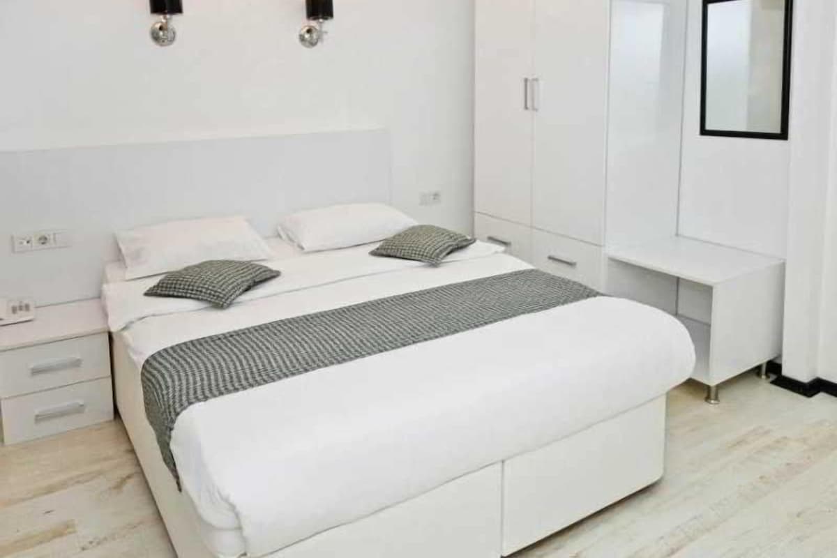 A modern bedroom with a large bed, white wardrobe, and wall-mounted lighting.