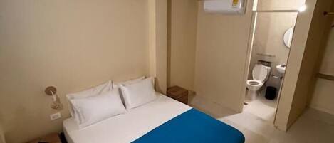 A bedroom with a bed, a nightstand, a bathroom with a toilet and a mirror.