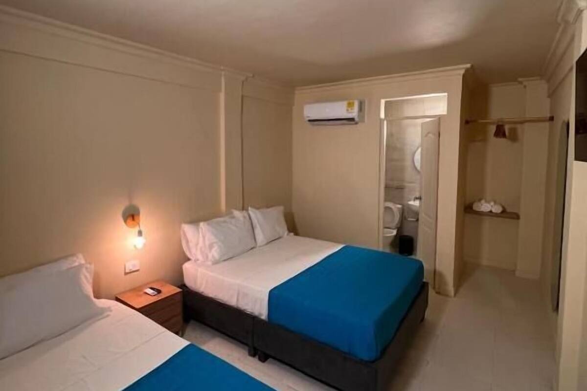 A hotel room with two beds, a nightstand, an air conditioning unit, and a bathroom visible through an open door.