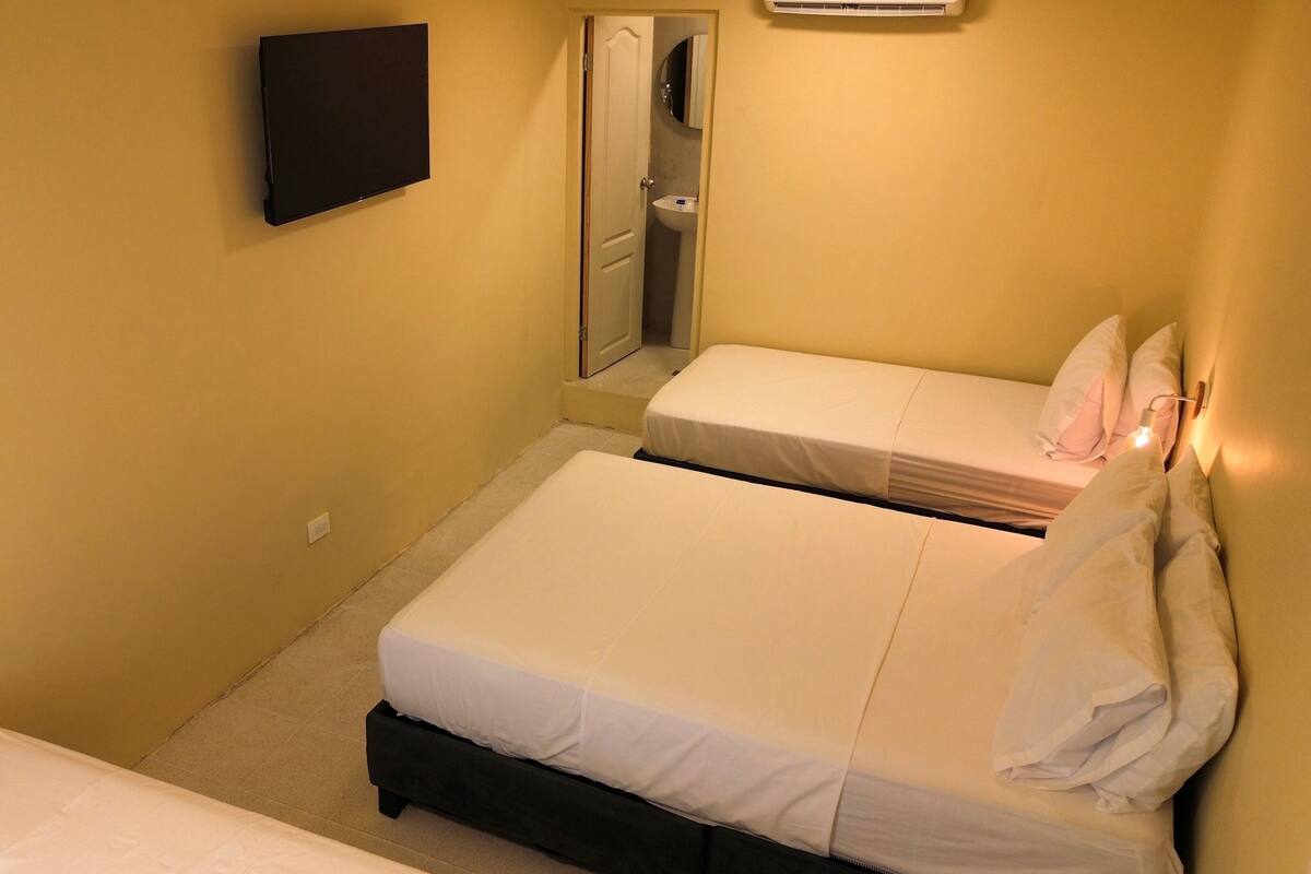 A small, single-room hotel bedroom with two beds, a flat-screen TV, and a bedside table.