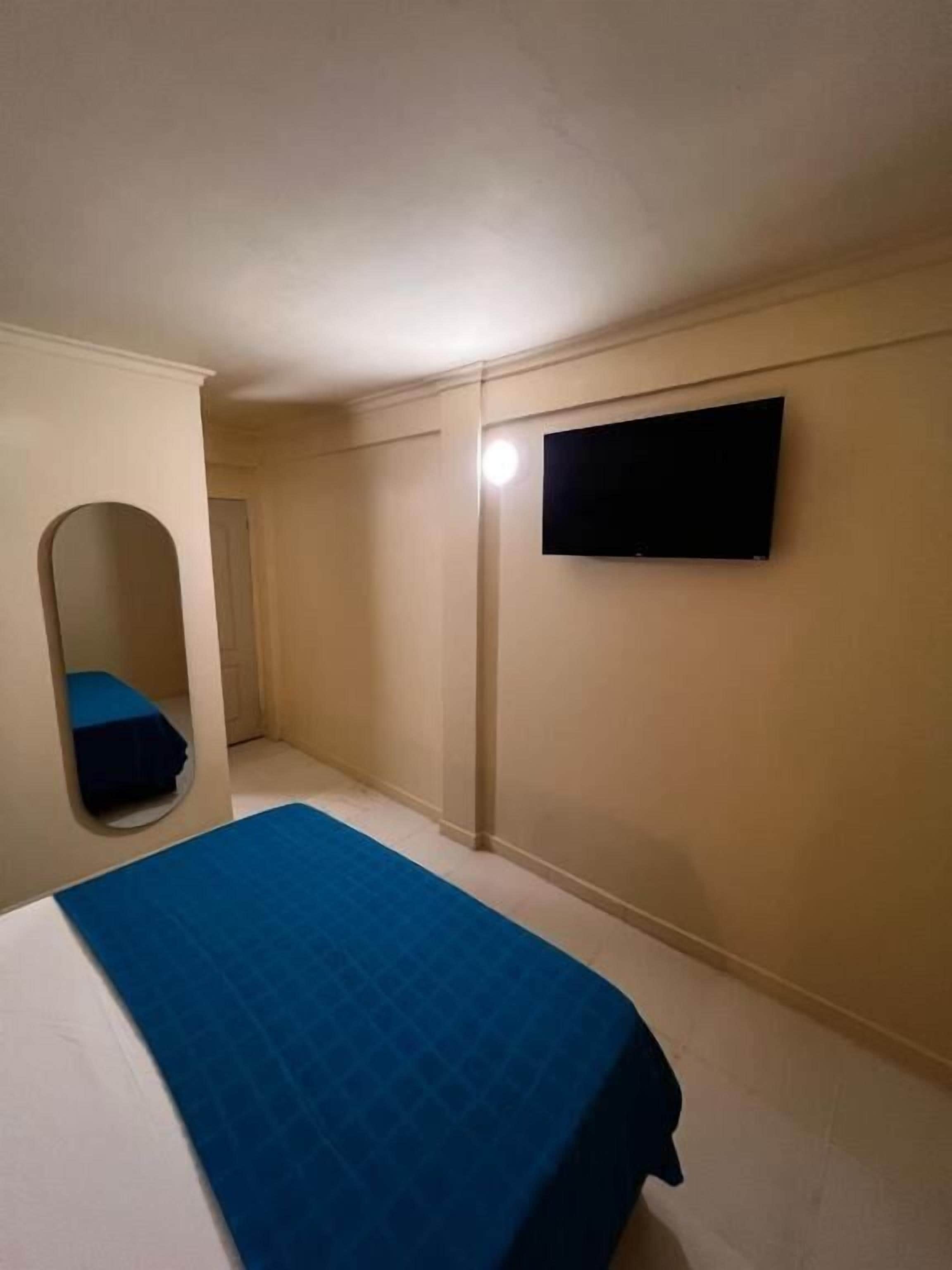 A bedroom with a bed, a TV mounted on the wall, and a door leading to another room.