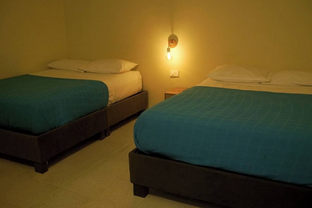 Two single beds with teal bedding, a wall-mounted light, and a nightstand.