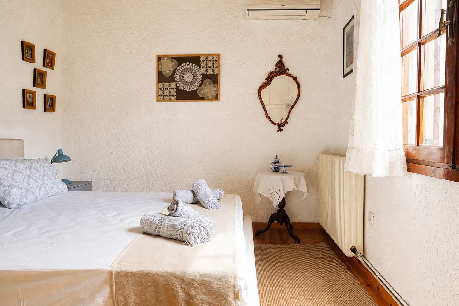 Une chambre à coucher avec un lit, une table de chevet, un miroir et une fenêtre avec des rideaux.