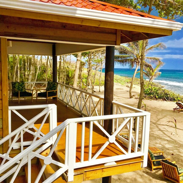 A wooden deck with white railings overlooking a beach with palm trees and ocean views.