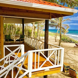 A wooden deck with white railings overlooking a beach with palm trees and ocean views.