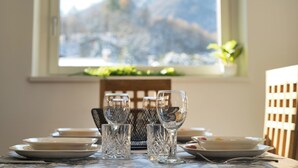 Ein Esstisch mit Tellern, Gläsern und Besteck vor einem Fenster mit Blick auf die Berge.