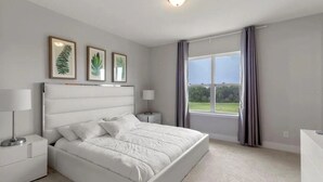 Une chambre à coucher comprenant un lit, deux tables de chevet, une commode, une fenêtre avec des rideaux et, au mur, des œuvres d’art représentant des feuilles encadrées.
