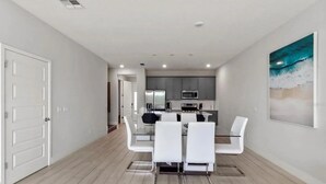 Une cuisine moderne avec des meubles gris, un four à micro-ondes et un coin repas comprenant des chaises blanches et une table en verre.