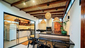 A modern kitchen with a glass partition, wooden ceiling, and a central island with chairs. - Casa DelMare Cond. com saída na praia (Buzios)