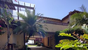 A courtyard with a paved walkway, palm trees, and a building entrance. - Casa DelMare Cond. com saída na praia (Buzios)