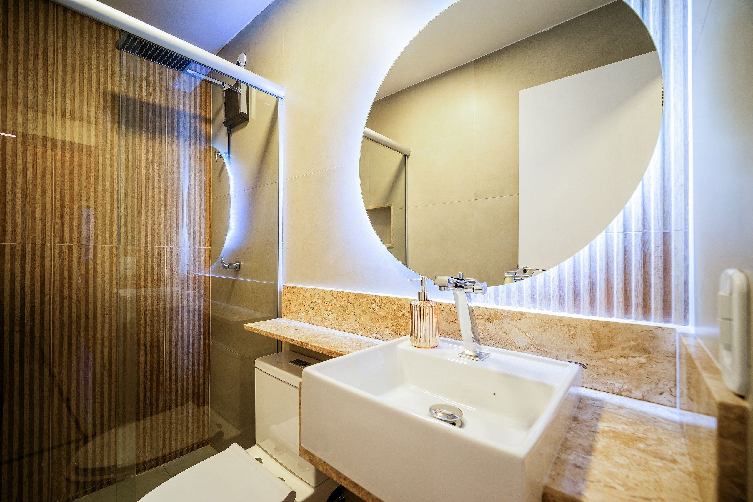 A modern bathroom with a large sink, a glass shower enclosure, and a round mirror.