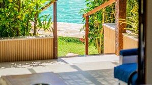 A view of a swimming pool surrounded by lush greenery, with a wooden deck and a covered seating area. - Casa DelMare Cond. com saída na praia (Buzios)