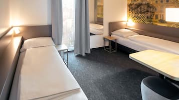 Habitación de hotel con dos camas individuales, una mesita pequeña, una silla y un ventanal con cortinas.