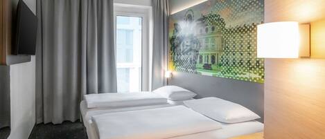 A hotel room with two beds, a large window with curtains, a wall-mounted TV, and a painting of a building.