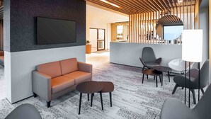 A modern lobby with a sofa, chairs, a TV, and a bar area. - B&B Hotel Würzburg-Altstadt (Würzburg)