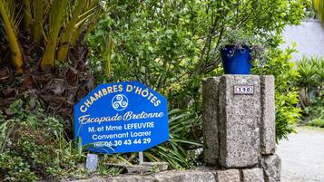 Une enseigne bleue indiquant « CHAMBRES D’HÔTES Escapade Bretagne », avec un pilier en pierre et une plante en pot.