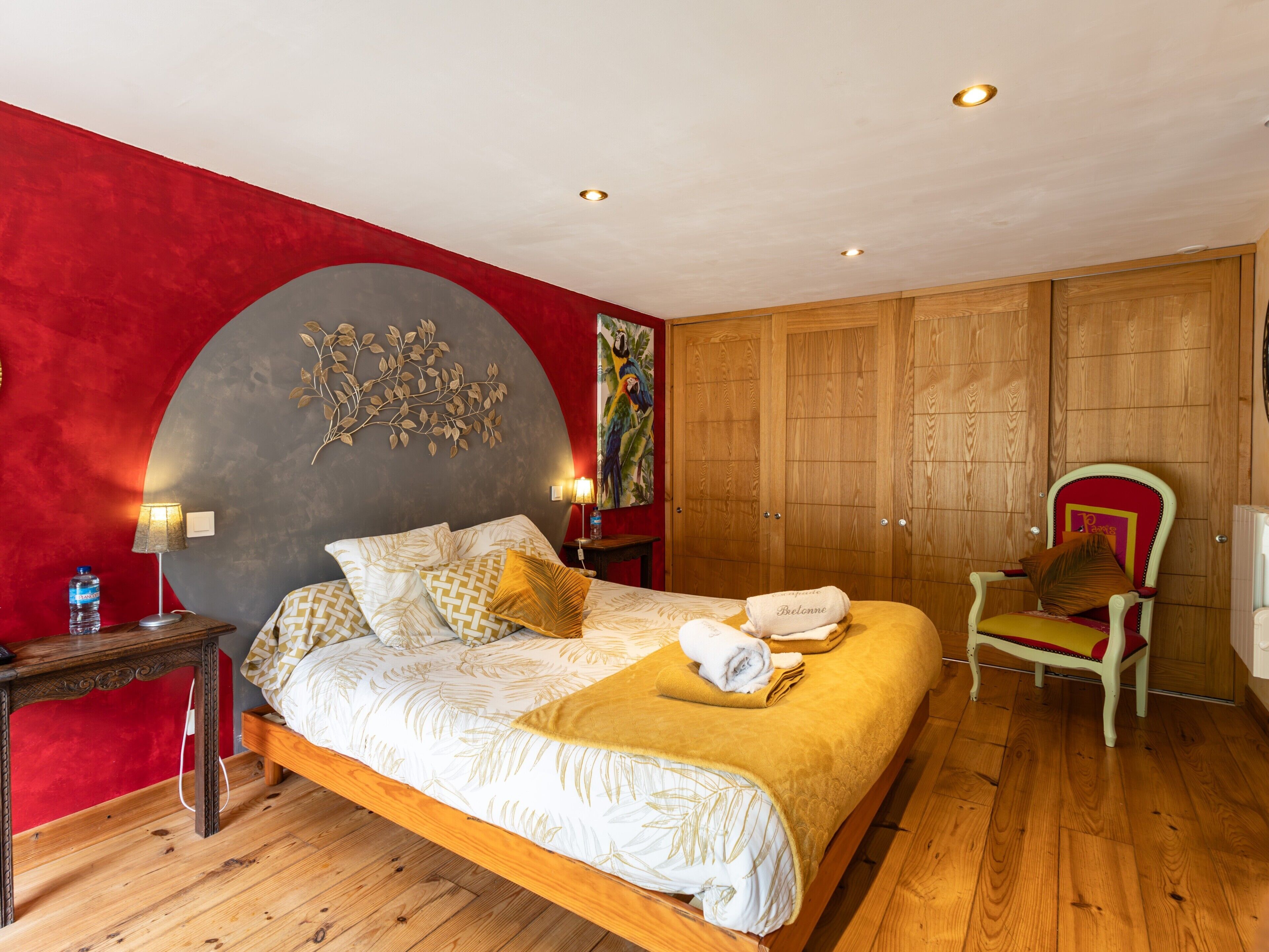 A bedroom with a bed, wooden wardrobe, a chair, and a wall art piece.